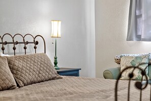Ein Bett mit gesteppter Bettdecke, ein Nachttisch mit Lampe und ein Sessel mit Blumenkissen.
