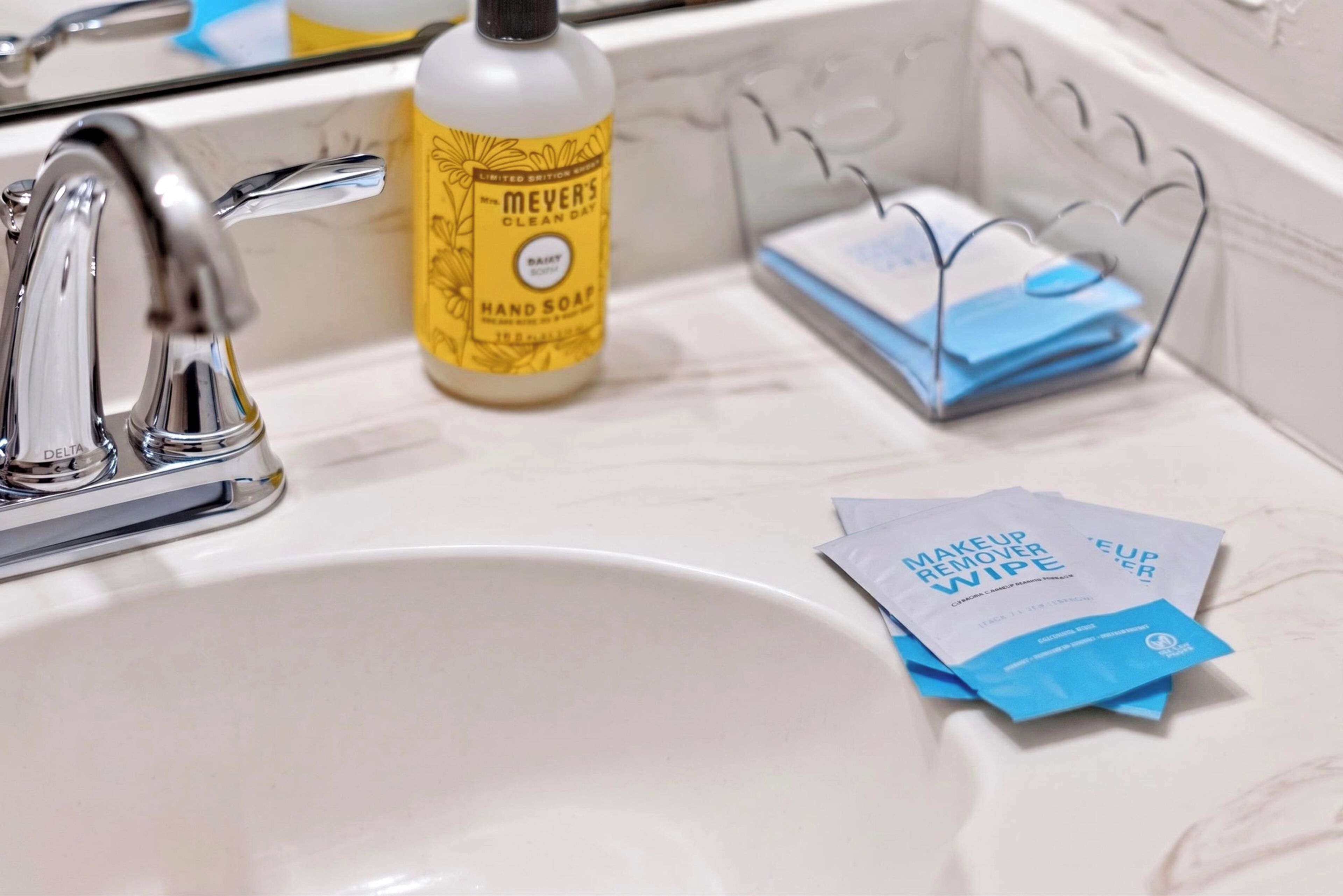 A bathroom sink with a faucet, a bottle of hand soap, and two makeup remover wipes.