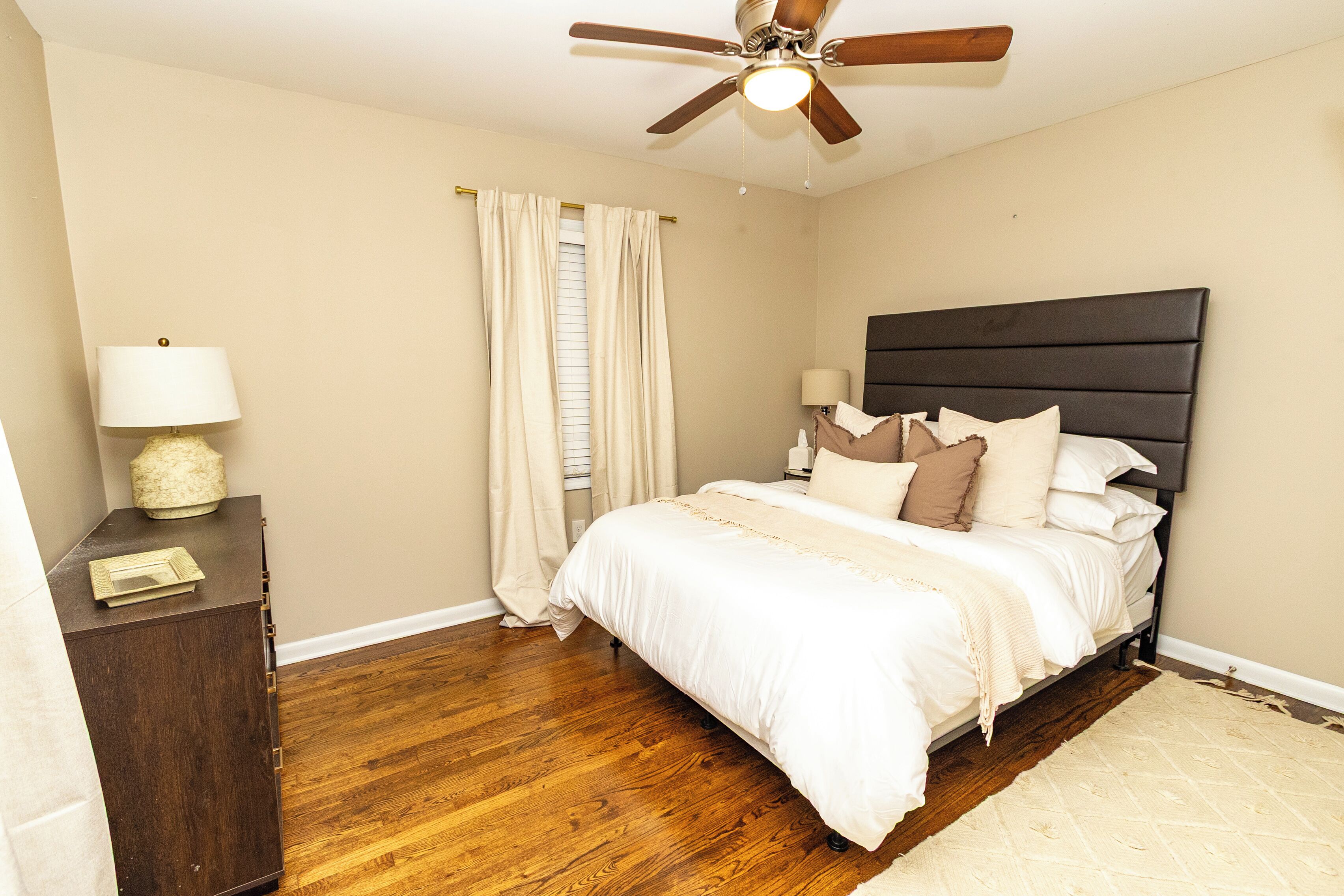 A bedroom with a bed, a ceiling fan, a nightstand, and a window with curtains.
