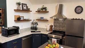 A modern kitchen with dark cabinetry, a stainless steel range hood, a built-in oven, and a refrigerator. -     1780 Post & Beam Studio - Historic Charm Near Downtown Keene (Keene)