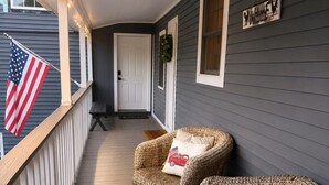 A covered porch with two wicker chairs, a flag, and a welcome sign. -     1780 Post & Beam Studio - Historic Charm Near Downtown Keene (Keene)