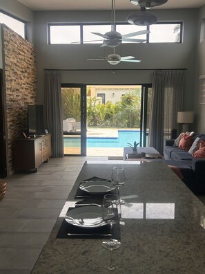 Ein modernes Wohnzimmer mit Essbereich, einer Steinwand, einem Deckenventilator und Blick auf einen Swimmingpool.