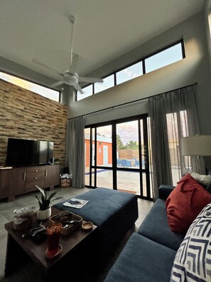 Ein modernes Wohnzimmer mit Steinwand, Flachbildfernseher, einer Couch, einem Couchtisch und einer großen Glasschiebetür, die zu einem Außenbereich führt.