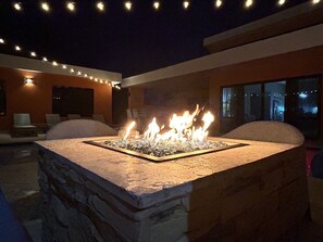 A stone fire feature with flames, surrounded by outdoor seating and string lights. - Casa Mal'Aud Private Tropical Casa Linda Oasis (Sosua)