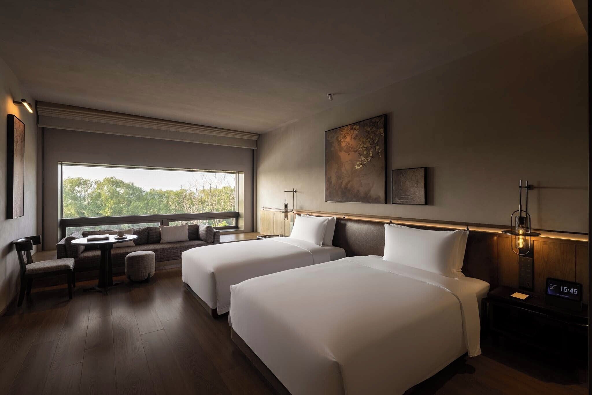 Ein Hotelzimmer mit zwei Betten, einer Sitzecke, einem großen Fenster und einem an der Wand befestigten Kunstwerk.
