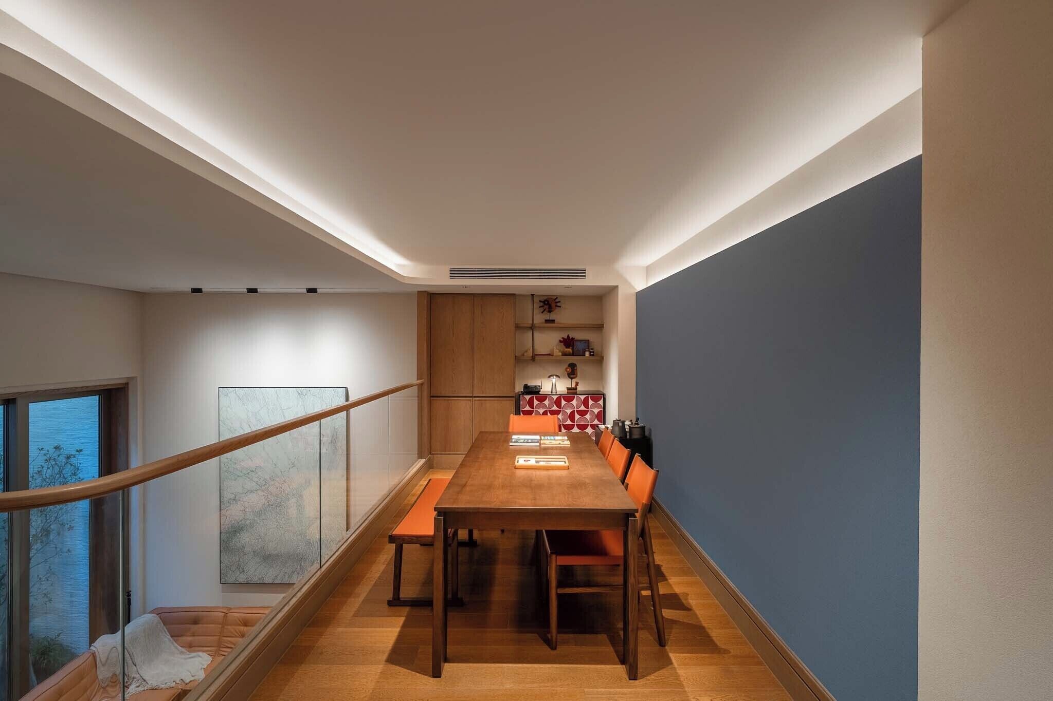 Un comedor con mesa y sillas de madera, una escalera y vistas al exterior.