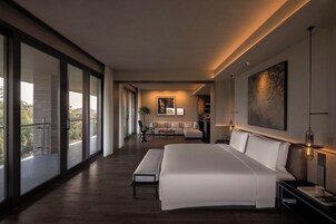 Una habitación de hotel moderna con una cama grande, una zona de estar con sofá y sillones, y un balcón con puertas de vidrio.