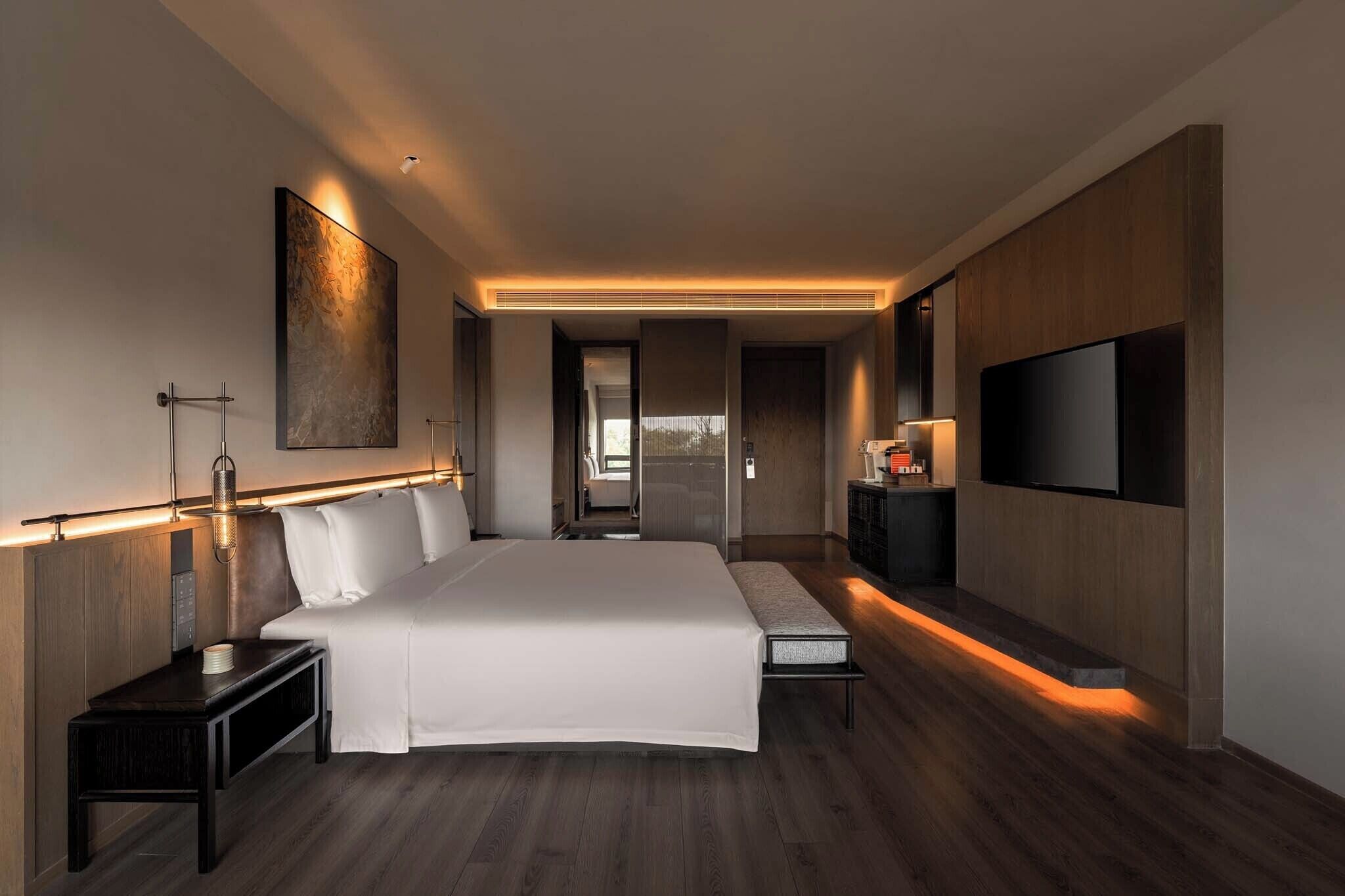 Een moderne hotelkamer met een groot bed, nachtkastjes, een flatscreen televisie en zicht op de aangrenzende kamer.