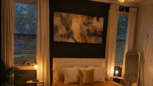 Ein Schlafzimmer mit einem Bett, einem Deckenventilator, einem Bild an der Wand und einem Fenster mit Vorhängen.