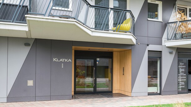 Ein modernes Geb äude mit Glastür, Holztür und einem Schild mit der Aufschrift 'KLATKA'.