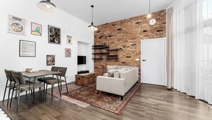 Een moderne woonkamer met een geaccentueerde bakstenen muur, een eetgedeelte met een tafel en stoelen, en een bank.
