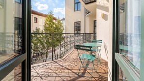 Een balkon met een patroon vloer, een groene tafel en stoelen, en uitzicht op omliggende gebouwen en bomen.