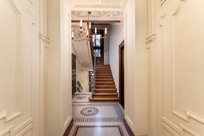 Um corredor com escada de madeira, piso estampado e teto decorativo.