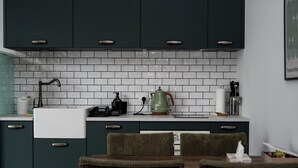 Een keuken met donkere kasten, een witte betegelde spatwand, een koffiezetapparaat en een eethoek met stoelen.