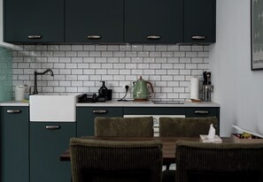 Eine Küche mit dunklen Schränken, einer weißen Fliesenrückwand, einer Kaffeemaschine und einem Essbereich mit Stühlen.