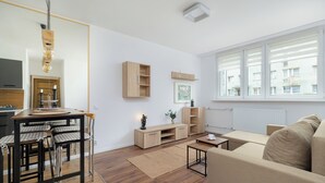 Ett modernt vardagsrum med en soffa, ett matbord med stolar, ett soffbord och ett stort fönster med persienner.