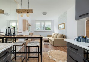 Una cocina moderna con taburetes de bar, una mesa de comedor y un sofá en un salón luminoso con ventanas amplias.