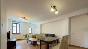 Un grand espace de vie doté d’un plancher en bois, d’une table à manger avec des chaises, d’un canapé et d’un téléviseur.