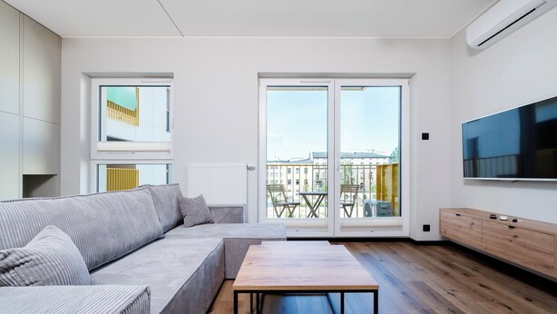 Ein modernes Wohnzimmer mit einer Couch, einem Holztisch, einem Fernseher und einem Balkon mit Gartenmöbeln.