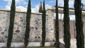 Un mur de pierre, bordé d’arbres hauts et étroits, et une porte en métal.