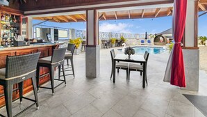 Een terras met een bar, rieten stoelen en een zwembad op de achtergrond.