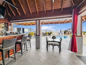 Ein Außenbereich mit Bar, Korbstühlen und einem Pool im Hintergrund.