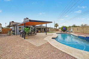 A residential backyard with a swimming pool, patio furniture, and a covered outdoor seating area. - Heated Private Pool at no extra charge, Arcade & BBQ, Prime N. Phoenix Location! (Phoenix)