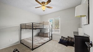 A bunk bed room with a ceiling fan, a window with blinds, a desk with a lamp, and a giraffe-patterned pillow. - Privat Pool w/ Diving Board, Arcade & BBQ, Prime N. Phoenix Location! (Phoenix)