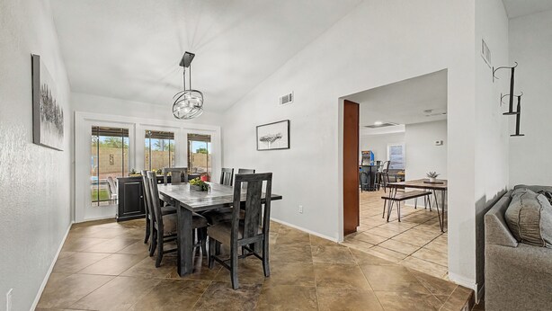 A spacious dining area with a large table and chairs, a kitchen in the background, and a living area with a couch. - Privat Pool w/ Diving Board, Arcade & BBQ, Prime N. Phoenix Location! (Phoenix)