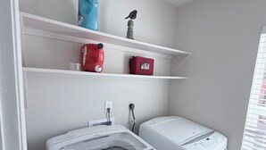 A laundry room with two front-loading washing machines, a shelf with a blue bottle, a red bag, and a bird figurine. - Privat Pool w/ Diving Board, Arcade & BBQ, Prime N. Phoenix Location! (Phoenix)