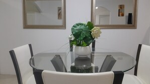 Et rundt glasbord med en hvid vase med en plante og en hvid blomst, omgivet af hvide stole.