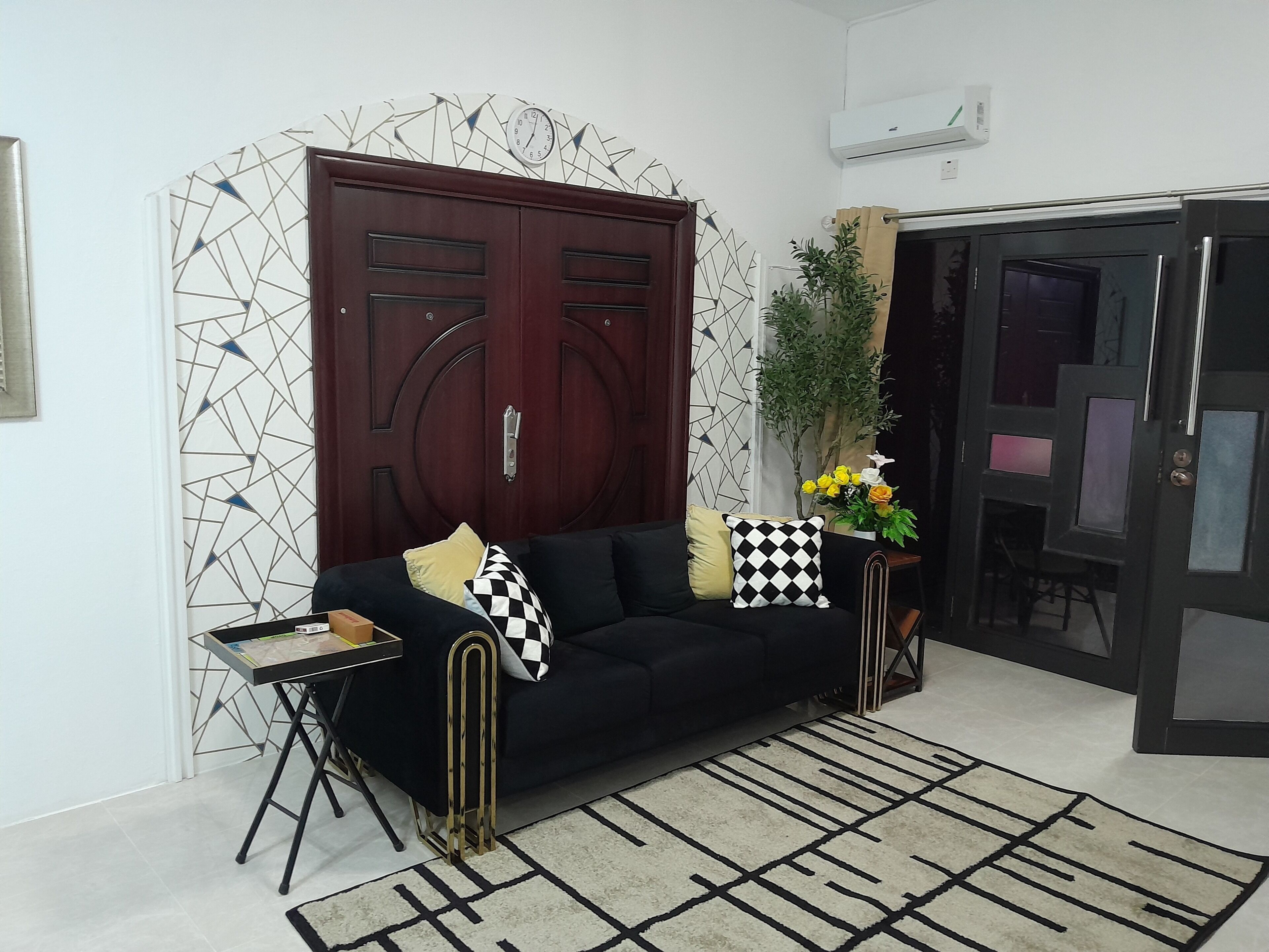 Un salon avec un canapé noir, un mur à motifs et une plante en pot.