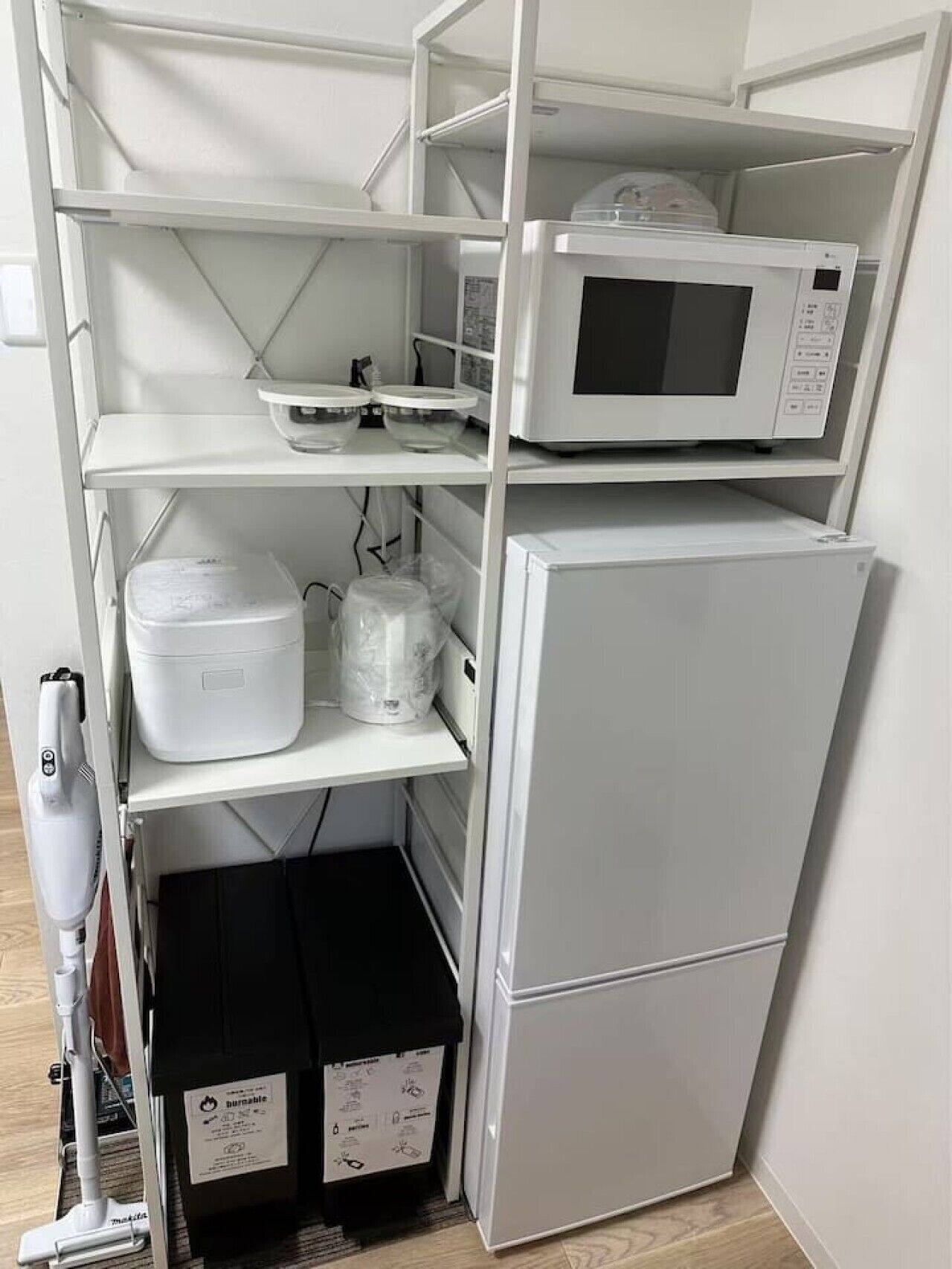 A compact kitchen with a microwave, a refrigerator, and storage shelves.