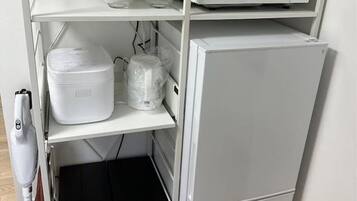 A compact kitchen with a microwave, a refrigerator, and storage shelves.