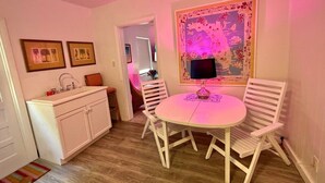 Quarto com uma mesa redonda, cadeiras brancas, um armário branco e uma obra de arte colorida na parede.
