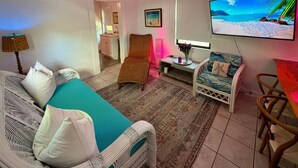 Quarto com cama, cadeira, mesa, televisão e vista para a praia.