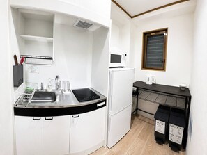 Eine kleine Küche mit Mikrowelle, Kühlschrank, Spüle und einer schwarzen Arbeitsplatte.