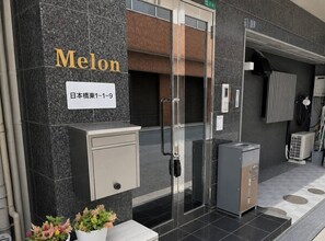 Ein Hotel Eingang mit Glastür, einer Namensschild, einer kleinen Vitrine und einem Blumentopf.