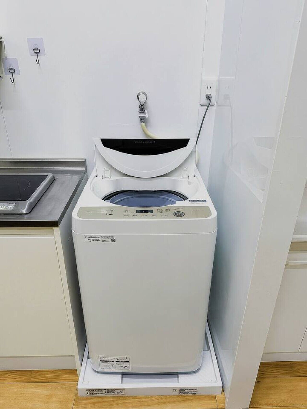 A compact, white washing machine with a control panel, placed on a wooden floor in a kitchen setting.