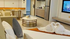 A modern hotel room with a sofa, a round coffee table, a TV, a kitchen area, and a dining table. - Wealth Mansion (Phnom Penh)