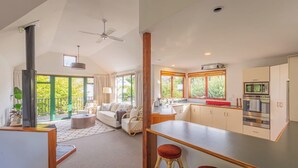 Eine moderne Küche mit Kochinsel, ein Essbereich mit hohem Tisch und Barhocker sowie ein Wohnzimmer mit Sofa und Kamin.