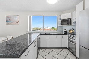 Una cocina moderna con un ventanal grande, electrodomésticos de acero inoxidable y piso de baldosas.