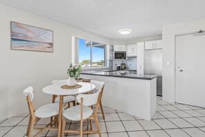 Una cocina moderna con armarios blancos, una isla central y un comedor con sillas blancas.