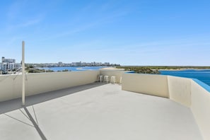 Una terraza en la azotea con vistas despejadas de un paisaje urbano costero, que incluye edificios y una playa.