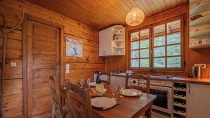 A wooden interior with a dining table set for four, a kitchen area with wine storage, and a large window with a view of greenery. - Chalet Petit Poucet 2BR Retreat in forest, Le Tour (Argentière), France (Le Tour (Argentière))