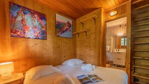 A wooden room with a bed, two paintings, a nightstand, and a night lamp. - Chalet Petit Poucet 2BR Retreat in forest, Le Tour (Argentière), France (Le Tour (Argentière))