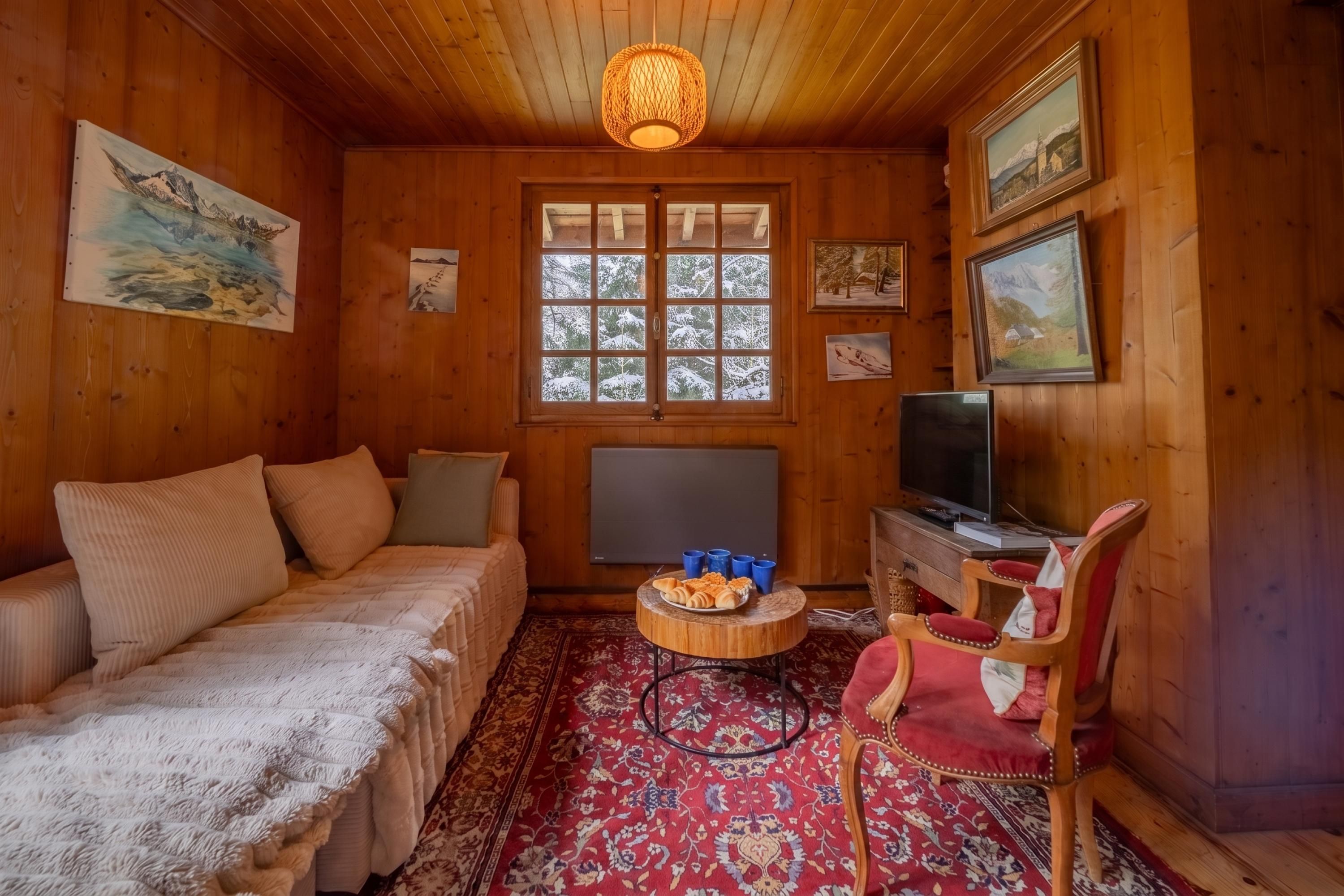 A cozy wooden room with a bed, a television, and a small table with pastries.