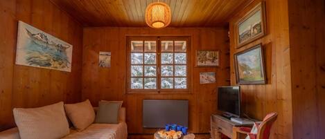 A cozy wooden room with a bed, a television, and a small table with pastries.