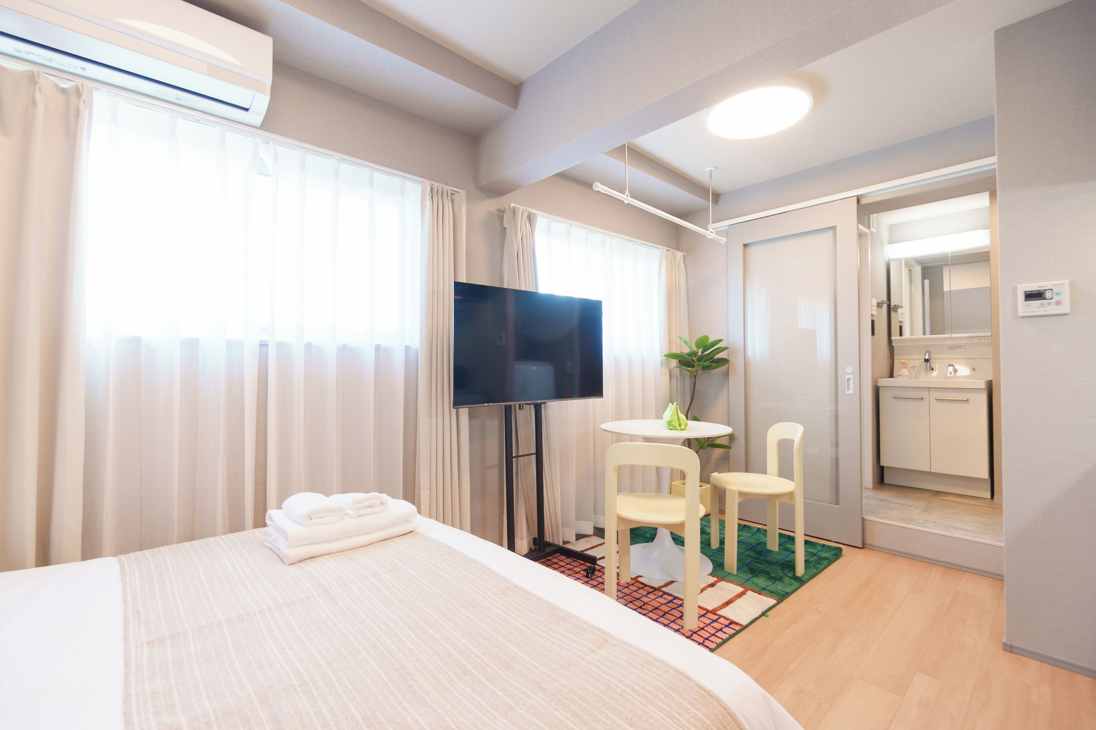 Habitación de hotel con cama, televisor, una pequeña mesa con sillas, baño con espejo y aire acondicionado.