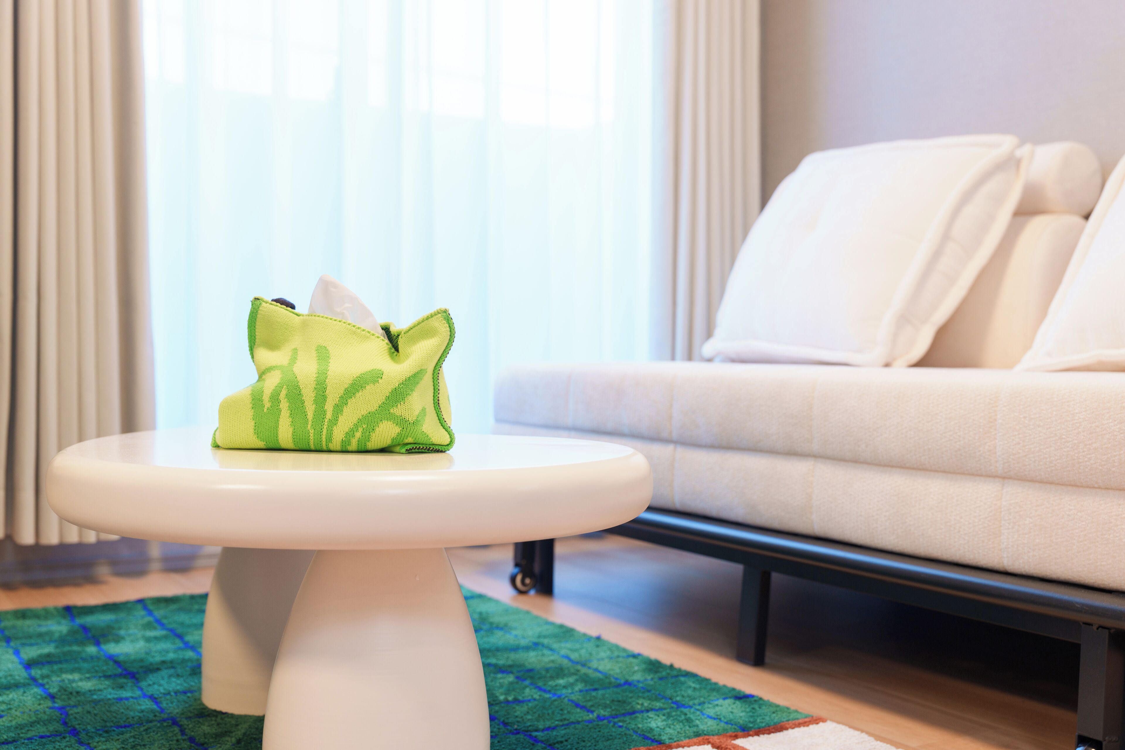 A white sofa, a green and white cushion, and a white table in a room with a patterned rug.